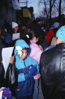 Picture of young boy in a crowd holding next to a person holding two flowers